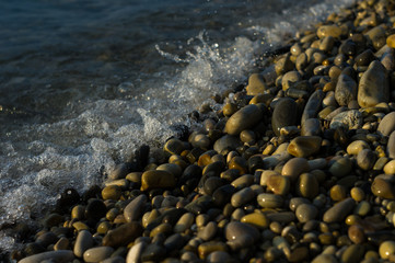 pebble stones on the sea beach, the rolling waves of the sea with foam