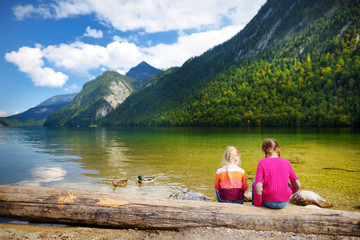 Two cute sisters enjoying the view of deep green waters of Konigssee, known as Germany's deepest and cleanest lake, located in the extreme southeast Berchtesgadener Land, Germany