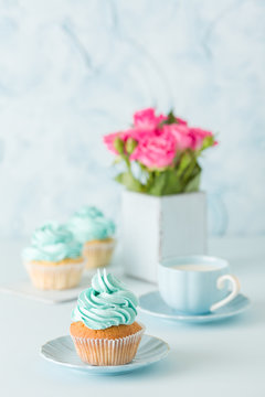Blue pastel vertical banner with decorated cupcakes, cup of coffe with milk and bouquet of pink roses.