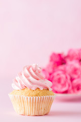 Cupcake with pink cream decoration and roses on pink pastel background.