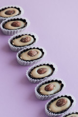 Row of delicious praline sweets with almonds on purple background