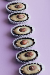 Row of delicious praline sweets with almonds on purple background