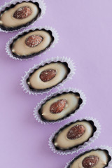 Composition of delicious praline sweets with almonds on purple background