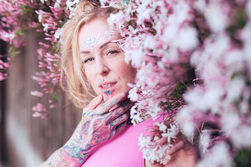 Fototapeta premium Tight portrait of blonde caucasian woman with tattoos near pink flowers