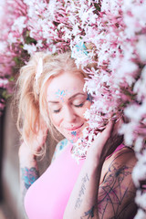 Fototapeta premium Tight portrait of blonde caucasian woman with tattoos near pink flowers