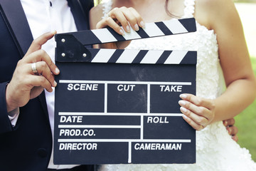 Happy beautiful bride and groom, woman holds clapper board, cinema board 