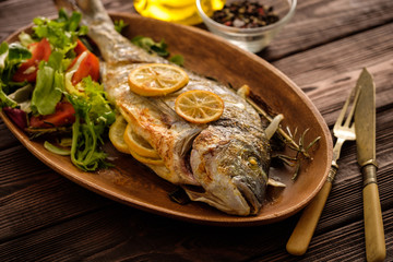 Grilled Dorado with lemon, thyme, rosemary and fresh salad on the wooden table.