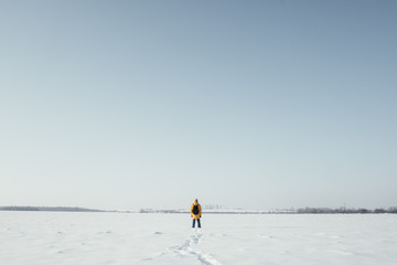 Fototapeta na wymiar Alone traveler in yellow jacket with black backpack on snowy winter field