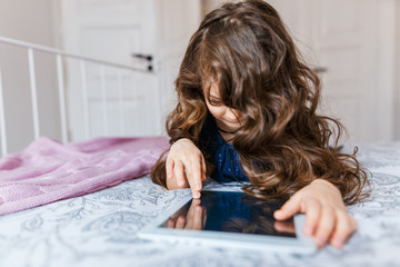 Cute little girl with curly hair using digital tablet