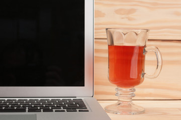 Open laptop with cup of tea on wooden background
