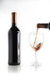 glass of red wine with full bottle on white background