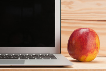 Open laptop with apple on wooden background