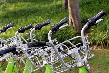 Fototapeta na wymiar Row bicycle handle bar and bell close-up, image of a bicycle rental in the city park sidewalk. Healthy, ecological transport concept