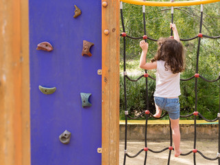 Little girl in blue shorts climbing rope ladder at playground in natural bushland setting (selective focus)
