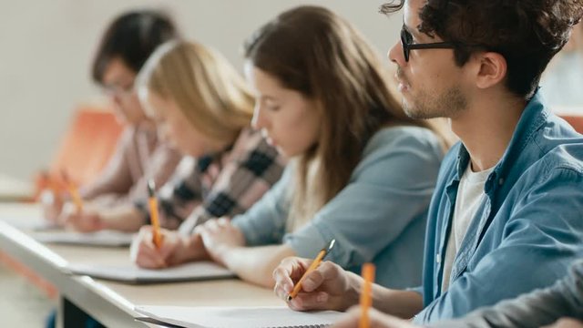 Row of Multi Ethnic Students in the Classroom Taking Exam/ Test/ Writing in Notebooks. Bright Young People Study at University. Shot on RED EPIC-W 8K Helium Cinema Camera.