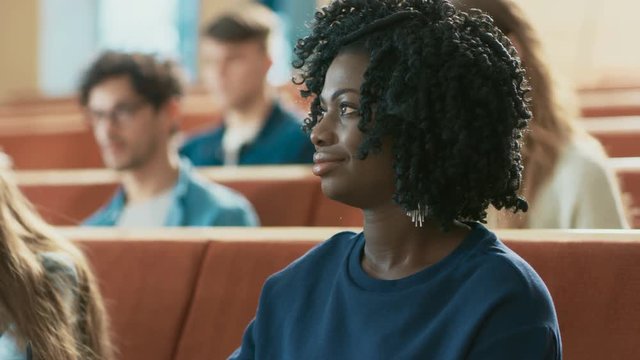 Close-up of a Beautiful Black Female Student Sitting Among Her Fellow Students in the Classroom, She's Writing in the Notebook and Listens to a Lecture. Shot on RED EPIC-W 8K Helium Cinema Camera.