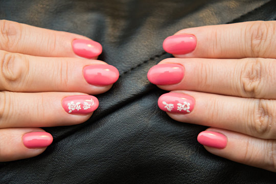 The nails are covered with pink gel Polish with a white sticker with a picture of a flower, located opposite each other