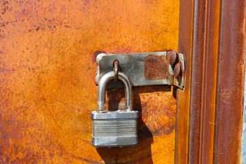 Silver padlock on old rusty door left unlocked where anyone can get in - vibrant colors of orange and brown rust