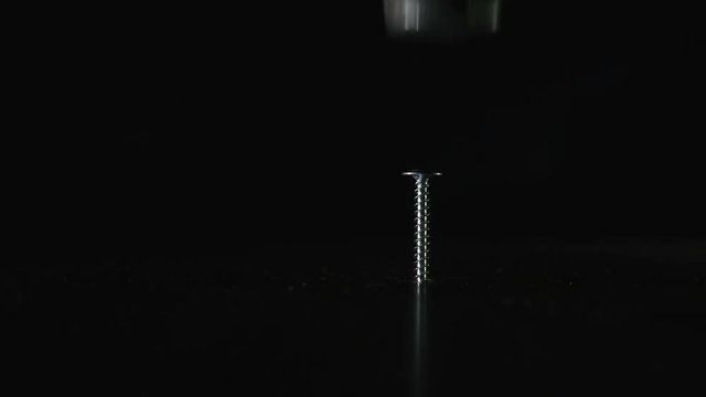 Screw is on a dark background. Hammer hits the screw, it bounces to the side. Close up. Concept: means does not correspond to the purpose, unreasonable use of force, force is-mind is not necessary, a