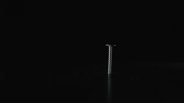 Screw is on a dark background. Hammer hits the screw, it bounces to the side. Close up. Concept: means does not correspond to the purpose, unreasonable use of force, force is-mind is not necessary, a