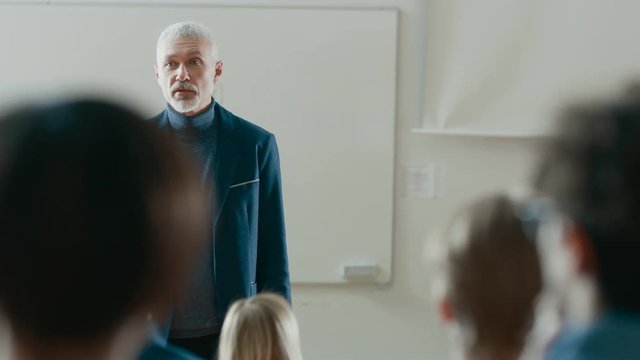 Back View of the Students in the Classrom Listening to a Prominent Professor Giving Lecture. Respectable Professor Holds Interesting Lecture. Shot on RED EPIC-W 8K Helium Cinema Camera.