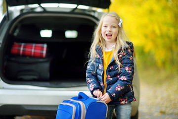 Adorable girl with a suitcase ready to go on vacations with her parents. Child looking forward for a road trip or travel. Autumn break at school.