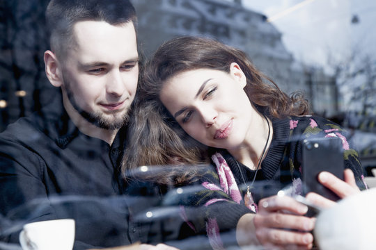 Young loving sensual couple taking selfie at cafe, view through a window