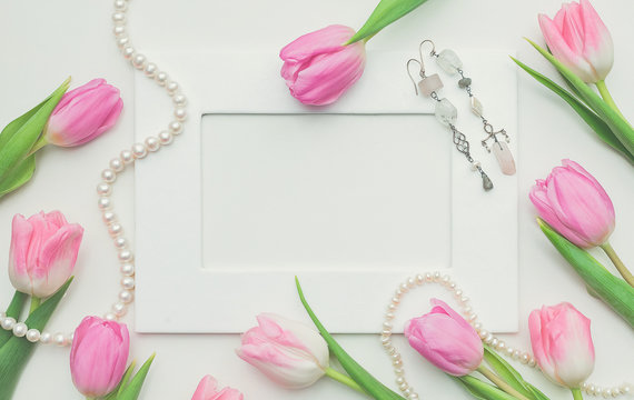 Pink tulips, photo frame, earrings and string of pearls on white background with copy space. Top view. Beautiful spring background for International Womens day, Mother's day, March 8, Valentines day