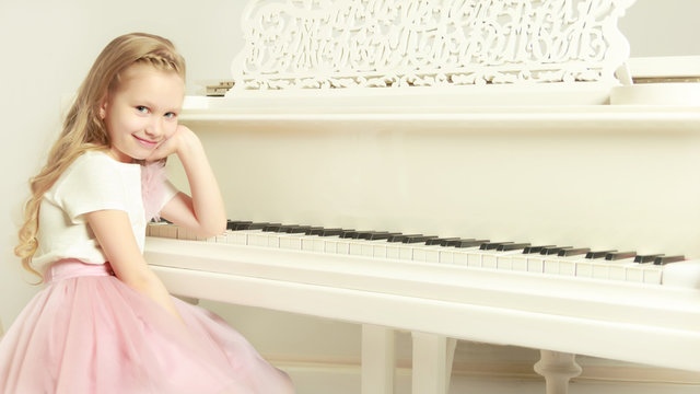 A little girl is sitting at the white piano.
