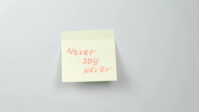 Closeup woman's hands stick yellow sticker paper sheets with words never say never.