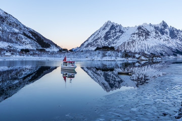 Winter landscape with boat in calm fjord, snowy mountains and re
