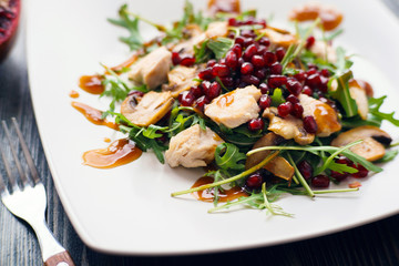 Appetizing chicken salad with pomegranate seeds and arugula on white plate, restaurant serving....