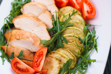Diet food, proteins, healthy low-calorie meals concept. Baked chicken breasts with zucchini, tomatoes and arugula, close up