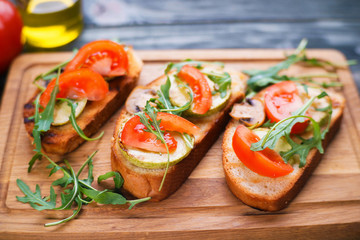 Delicious vegetarian snack bruschetta with chopped tomatoes and champignons, garnished with ricotta and basil, healthy homemade Italian antipasti top view on wooden table