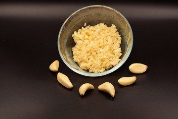 Chopped garlic in a glass bowl on a seamless black background. 