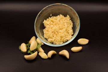 Chopped garlic in a glass bowl on a seamless black background. 