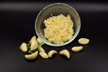 Chopped garlic in a glass bowl on a seamless black background. 