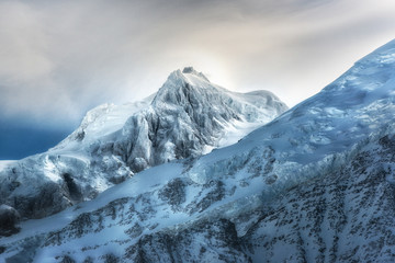 Obraz premium Góra wysokich gór, pokryta śniegiem. Zimowe góry w jasny słoneczny dzień. Alpejski krajobraz górski z pochmurnego nieba.