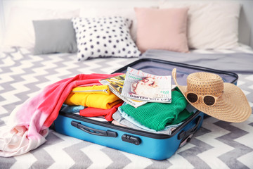 Open suitcase with different personal stuff on bed