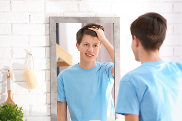 Teenage boy with acne problem looking in mirror at home