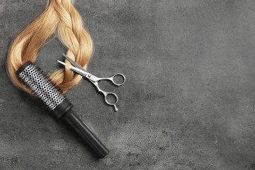 Professional hairdresser scissors, brush and strand of blonde hair on grey background, top view