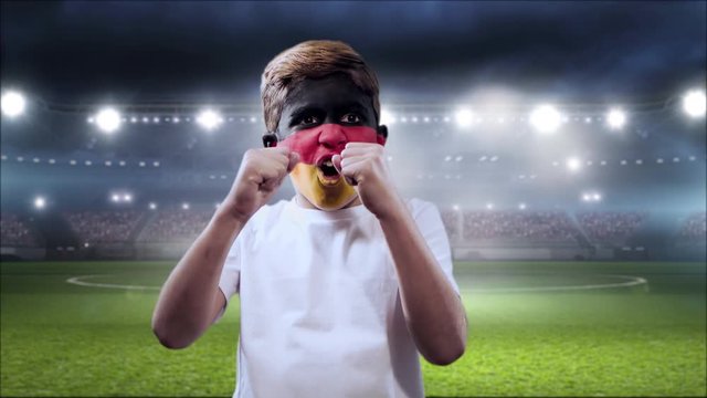 Boy screaming goal with his face painted with the German flag and stadium on the background