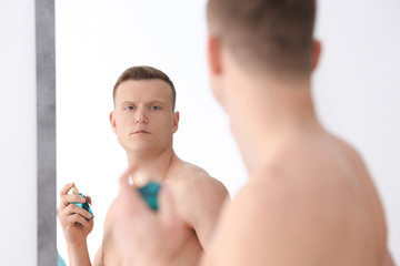 Fototapeta na wymiar Handsome man using perfume in front of mirror