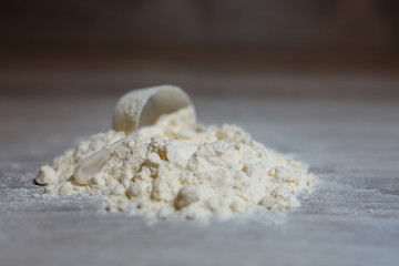 Close-up scoop in protein powder slides on a wooden table. bunch of protein powder with plastic spoon on white background. Dry mixture for dilution with milk or water. Sports dietary nutrition.