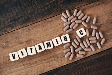 Vitamin C pills on wooden table with alphabet tiles written VITAMIN C. Healthcare and medical concept