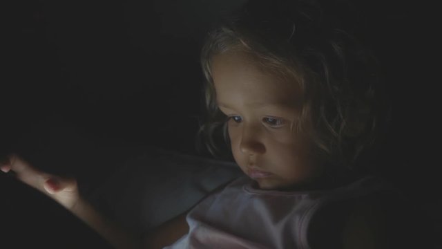 Portrait of little child girl using tablet technology in bed by night at home.