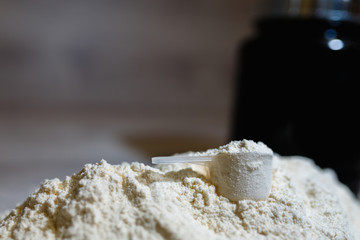 Photo of product spoon or measuring scoop of whey protein on black plastic jar background with lid on grey wooden background. Dry mixture for dilution with milk or water. Sports dietary nutrition.