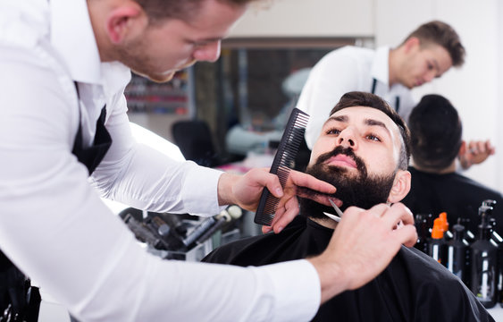 Positive man forming beard of client into shape