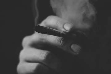 Smoke on a black background. A man smokes cannabis weed, a joint and a lighter in his hands....