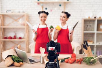 Two culinary bloggers hold up peppers and knives to camera.